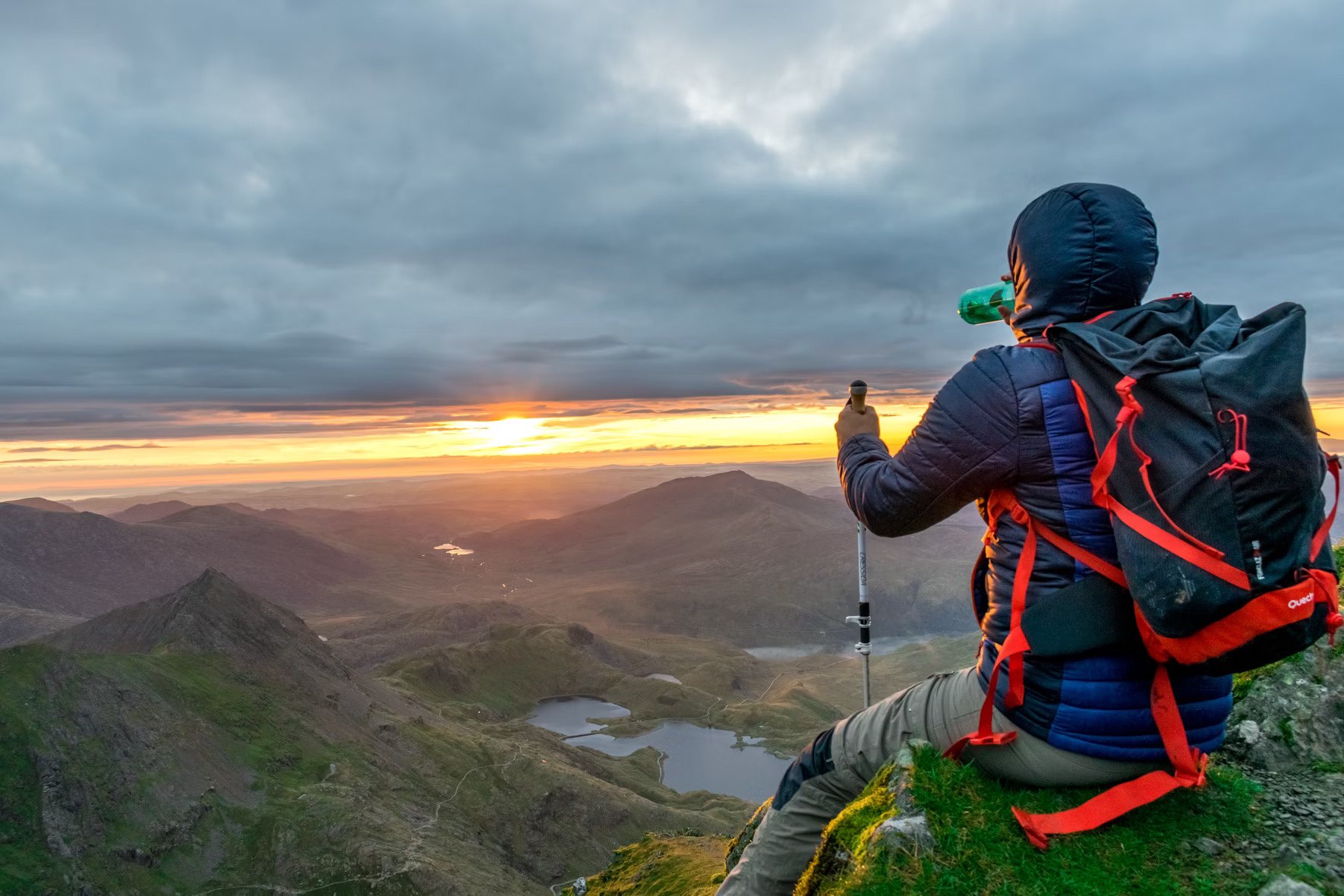 Photo of Hillwalker sitting on peak admiring sun setting over hills